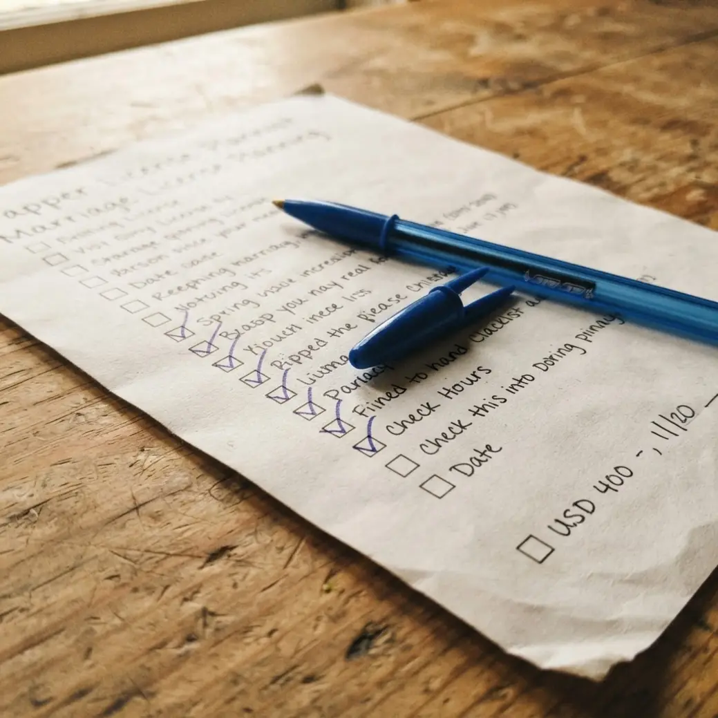Close-up of hands filling out marriage license requirements paperwork with a pen on a wooden desk